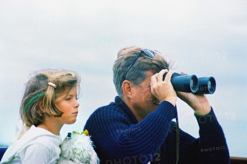 U.S. President John F. Kennedy looking through binoculars while sitting next to his daughter, Caroline Kennedy, aboard the Presidential yacht, “Honey Fitz,” off the coast of Hyannis Port, Massachusetts, USA, Cecil Stoughton, White House Photographs, August 25, 1963