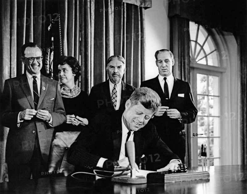 U.S. President John F. Kennedy signing joint resolution in support of Detroit's bid to host 1968 Olympic Games, in background: Michigan Senator Philip A. Hart, Representative Martha W. Griffiths, Representative Neil Staebler, and Representative Harold M. Ryan, Cabinet Room, White House, Washington, D.C., USA, Abbie Rowe, White House Photographs, September 16, 1963