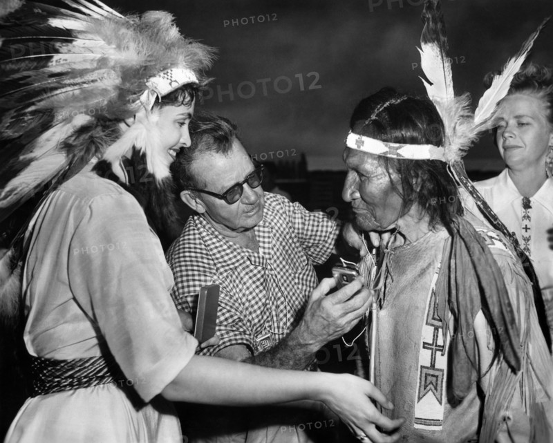 Suzan Ball (left), John Sitting Bull being given a hearing aid (left), on-set of the western film, "Chief Crazy Horse", Universal Pictures, 1955
