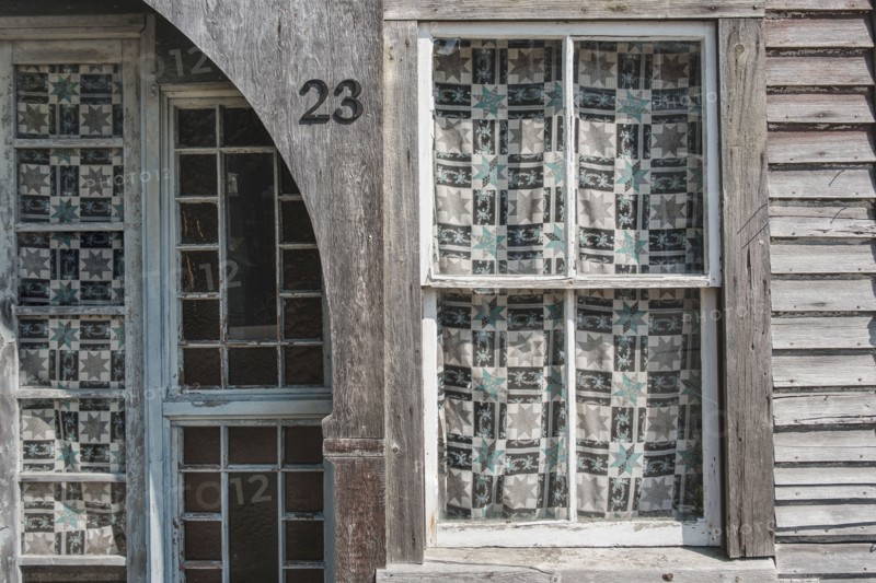 Weathered building exterior with pane windows covered in patterned curtains