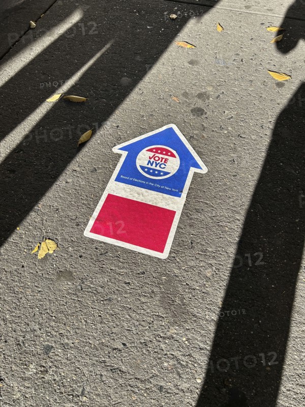 High angle view of human shadows near NYC board of elections early voting arrow sign adhered to pavement, New York City, New York, USA