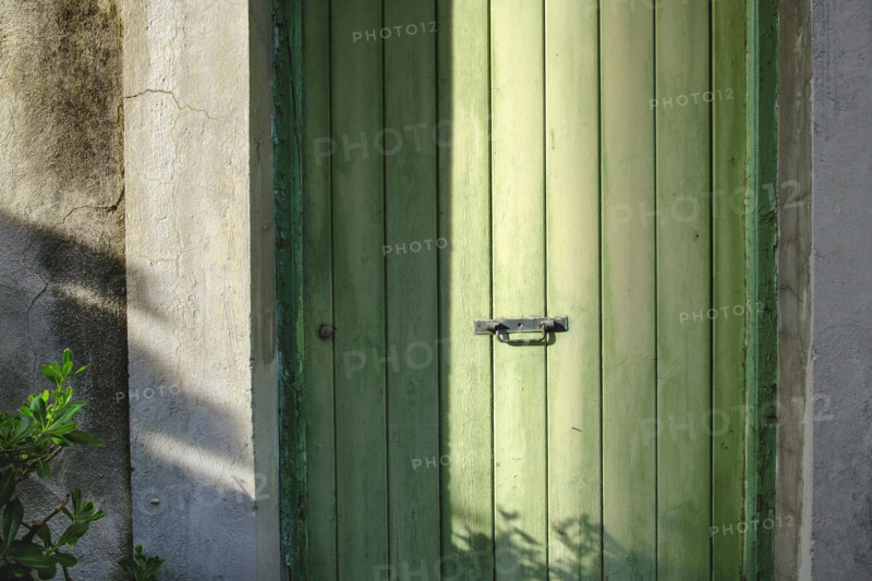 Old green wood door with center black metal handle in shadow