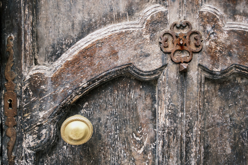 Weathered wood door with intricate carvings, rusted metal hardware and gold-colored door knob