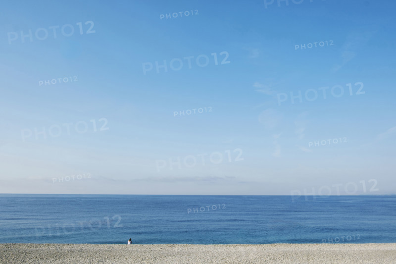 Rear view of solitary woman sitting on beach and looking out to sea