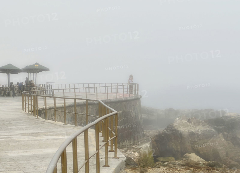 Group of people enjoying outdoor restaurant overlooking sea on misty morning