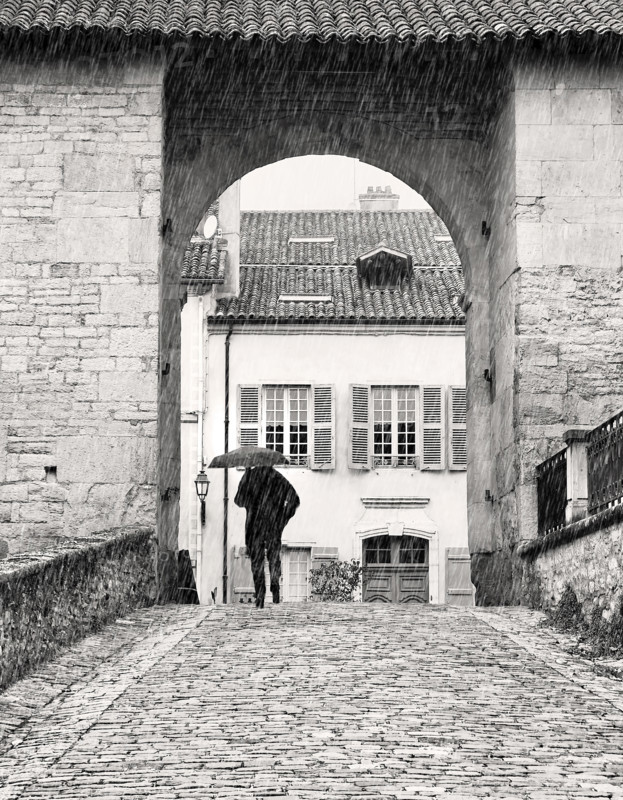 Man walking along cobblestone street in rain, Cluny, France
