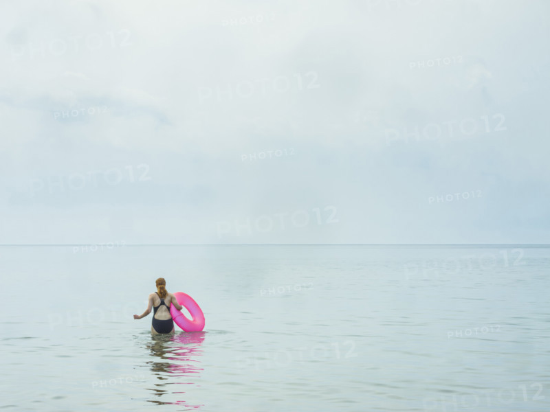 Rear view of young adult woman wading in water holding a pink inner tube