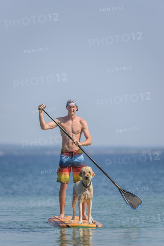 Teen boy with pet golden doodle on paddle board