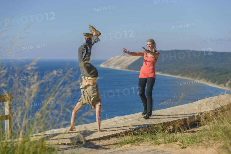 Young adult man performing handstand while young adult woman watches with arms extended forward