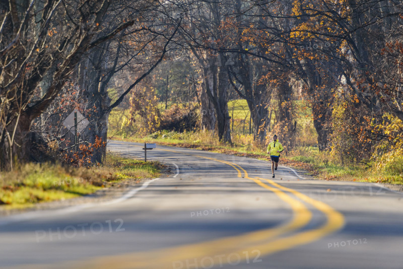 Mid-adult man running along scenic road in autumn