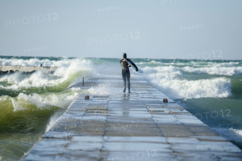 Rear view of surfer in wetsuit walking to end of pier