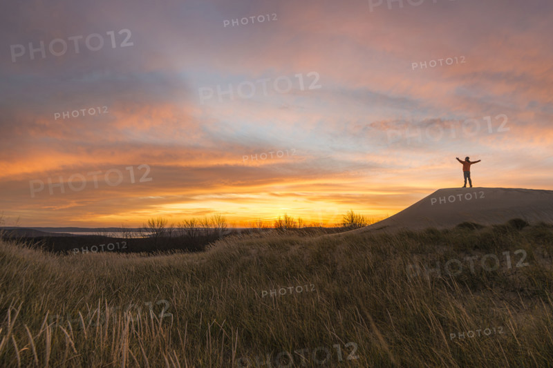 Silhouette of mid-adult man with raised arms greeting lakeside sunrise
