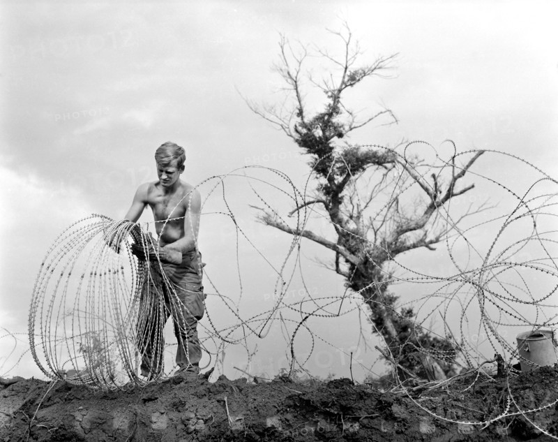 Member of 1st Brigade, 5th Infantry Division (Mechanized), taking down barbed tape (modified form of concertina wire) surrounding command post of Operation Utah Mesa, A Shau Valley, Vietnam, U.S. Army Signal Corps, July 1969