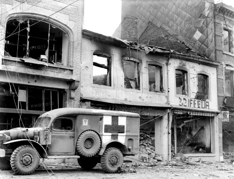 American ambulance waiting outside bombed building while a searcher looks for persons injured during ten-day defense by 101st Airborne Division, Bastogne, Belgium, U.S. Army Signal Corps, December 26, 1944