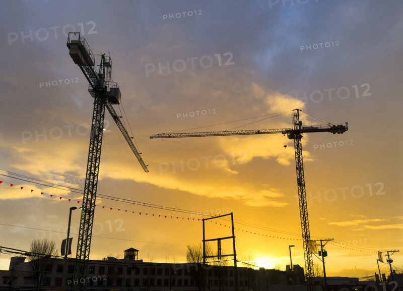 Two silhouetted construction cranes at sunset