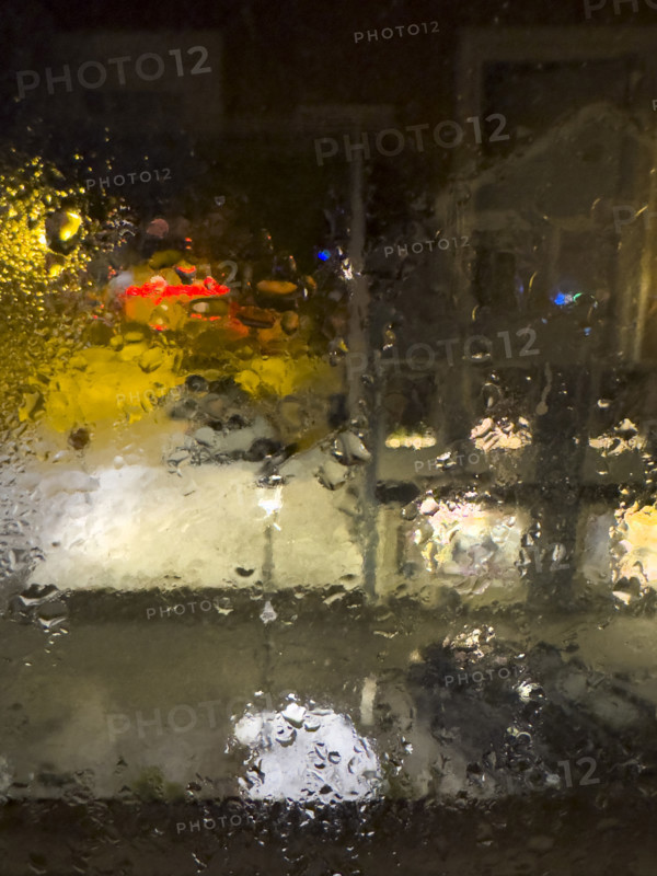 Blurred street scene viewed through window with dripping raindrops at night