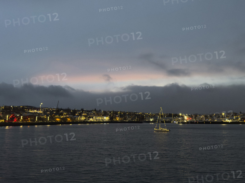 Sailboat with Christmas lights in harbor with illuminated seaside town in background, Hafnarfjordur, Iceland