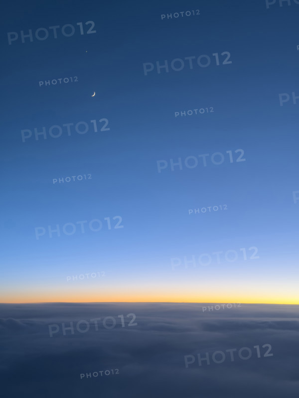 Crescent moon in deep blue sky at sunset viewed through airplane window