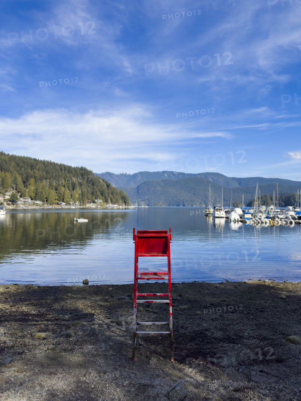 Red lifeguard chair on beach with houses on left and sailboats on right, Port Moody, North Vancouver, British Columbia, Canada