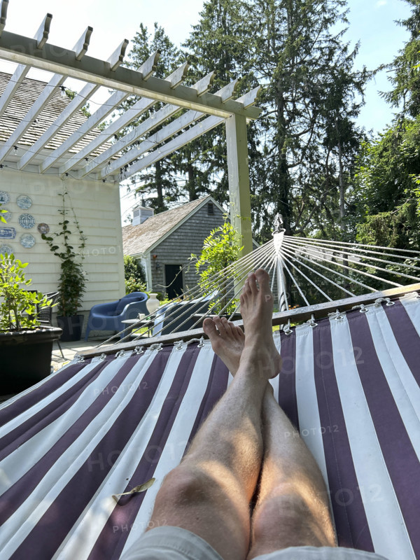 View of mid-adult man's bare legs and feet while relaxing in hammock on summer day