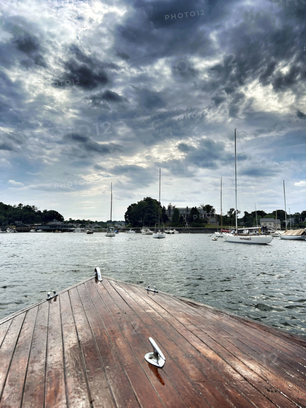 Bow of vintage wood boat with moored harbor sailboats in background