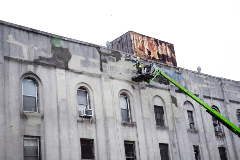 Workman repairing facade of old factory building, Brooklyn, NY, USA