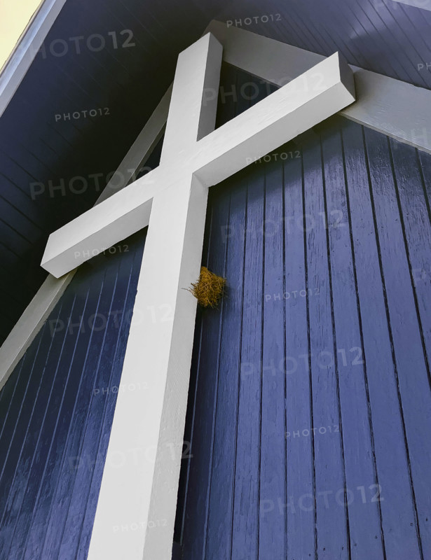 Bird nest tucked behind large white religious cross on building exterior, low angle view