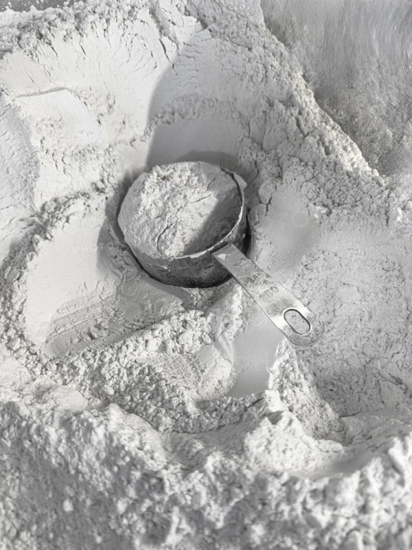 Full measuring cup of flour sitting in a mound of flour