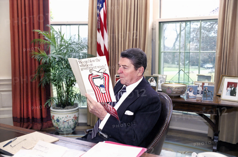 U.S. President Ronald Reagan reading a book "We can blow the whistle on Government waste" in the White House Oval Office, Washington, D.C., USA, President Ronald Reagan White House Photographic Office, December 19, 1984