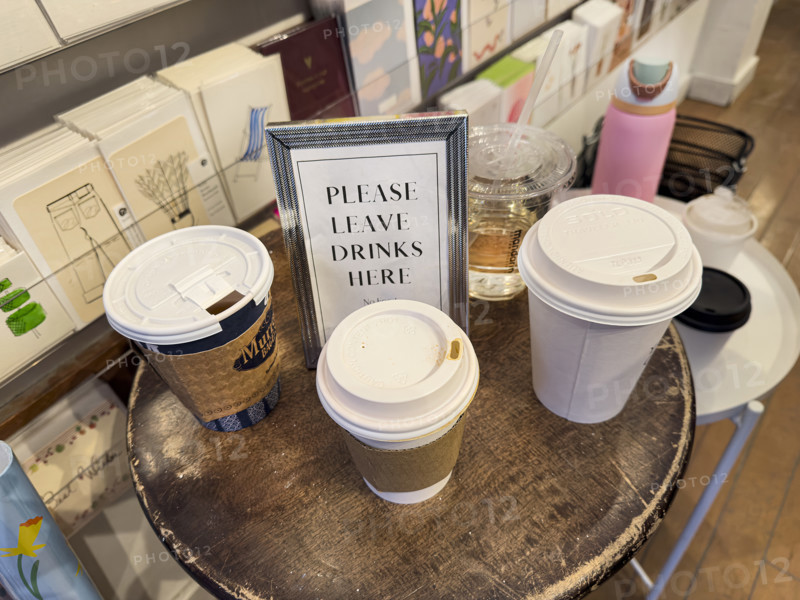 "Please leave drinks here" framed sign on round wood table with paper and plastic cups in retail store