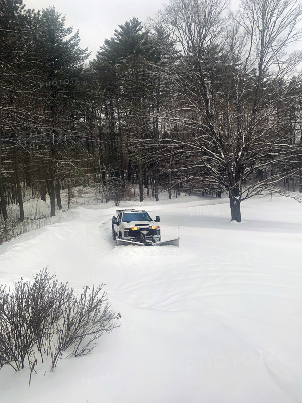 White pickup truck with plow attachment removing snow from residential driveway