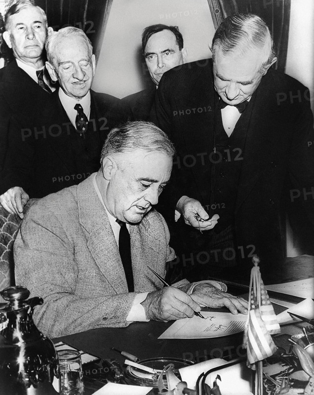U.S. President Franklin D. Roosevelt signing declaration of war against Germany, marking U.S. entry into World War II in Europe, as U.S. Senator Tom Connally holds watch to fix exact time of declaration with (L-R): Senator Alben Barkley (KY), Senator Carter Glass (VA), Representative Joseph Martin (MA), White House, Washington, D.C., USA, U.S. Office of War Information, December 11, 1941