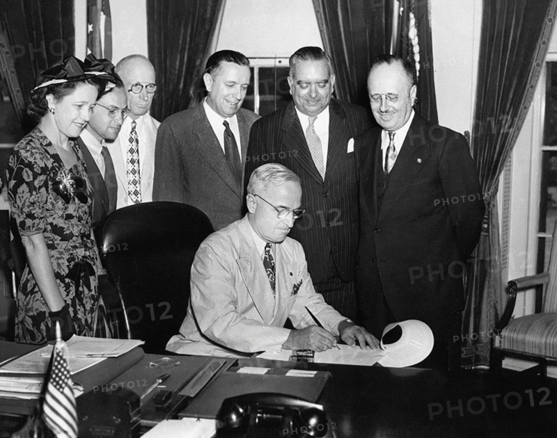 U.S. President Harry S. Truman (seated) in the White House Oval Office signing bill to make governorship of Puerto Rico an elected office as Governor of Puerto Rico Jesus T. Pinero (standing, 2nd right), and Puerto Rico Resident Commissioner Antonio Fernos Isern (standing right) look on, Washington, D.C., USA, Abbie Rowe, National Parks Service, Harry S. Truman Library, August 5, 1947