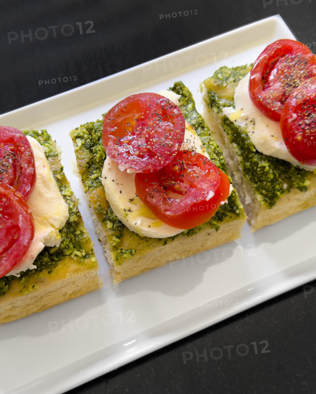 Tomato, mozzarella, basil and pesto and toasted bread on white plate