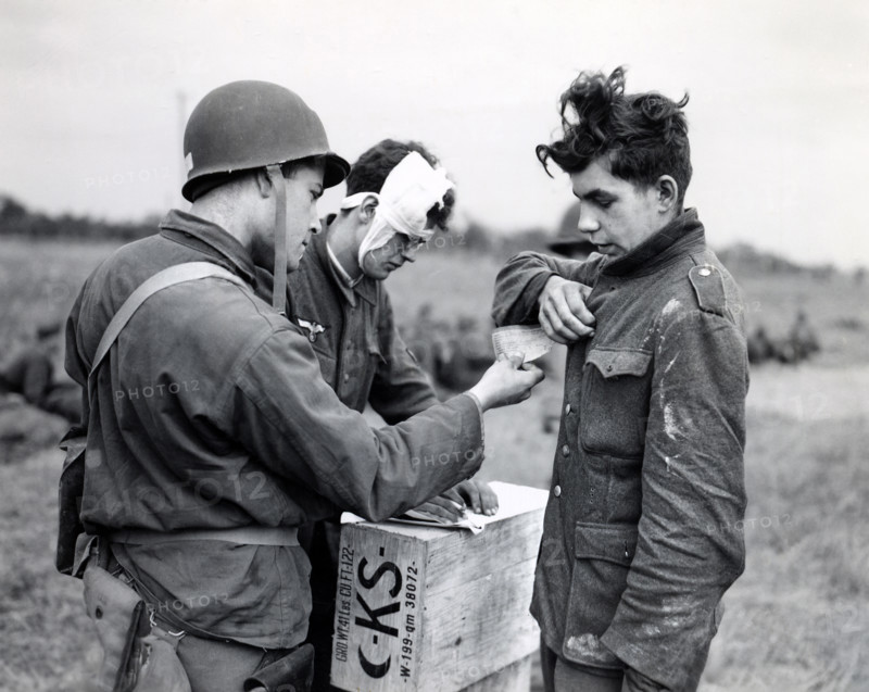 American soldier making out identity tag for young German prisoner of war as another wounded Nazi supplies necessary information, Normandy, France, U.S. Army Signal Corps, June 9, 1944