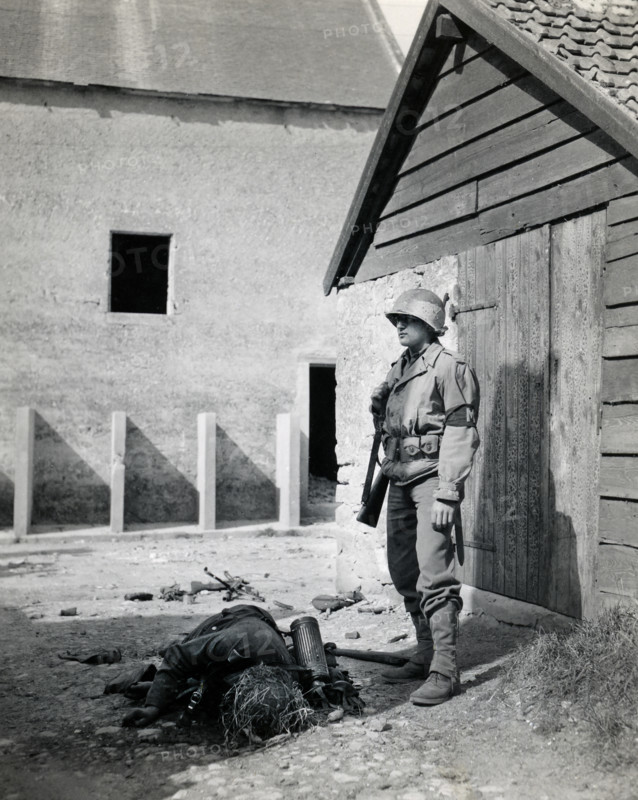 U.S. military police standing guard in barnyard near body of dead German sniper, Normandy, France, Bowen, U.S. Army Signal Corps, June 15, 1944