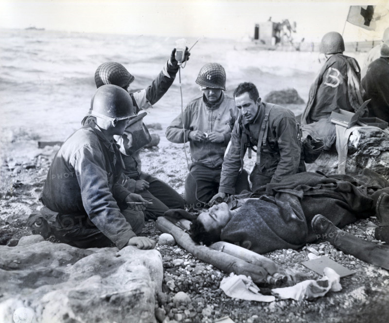 U.S. Army medical soldiers, just a few feet from the surf, administering plasma transfusion to survivor of sunk landing craft, Normandy, France, U.S. Army Signal Corps, June 1944