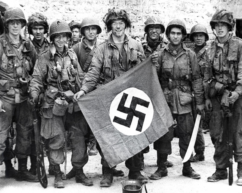 American paratroopers, among the first to make successful landings on European continent, holding Nazi flag captured in village assault, Utah Beach, Saint-Marcouf, Normandy, France, Werner, U.S. Army Signal Corps, June 8, 1944