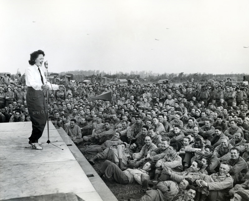 Crowd of GIs flock around an improvised platform to witness first U.S.O. camp show, France, U.S. Army Signal Corps, July 26, 1944