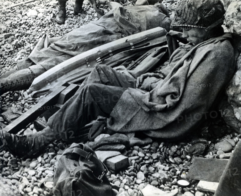 American soldier of 3rd Battalion, 16th Infantry Regiment, 1st Infantry Division, resting after storming ashore from landing craft, Omaha Beach, Colleville-Sur-Mer, Normandy, France, U.S. Army Signal Corps, June 6, 1944