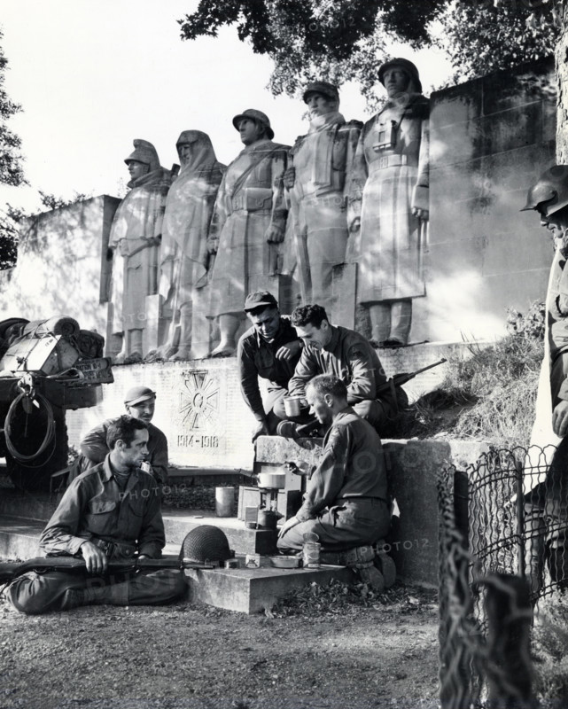 Group of American soldiers cooking dinner on GI stove under World War I memorial, near Verdun, France, U.S. Army Signal Corps, September 1, 1944