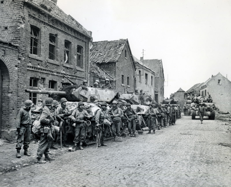Infantrymen of 1st Division, U.S. First Army, resting beside military tanks, Monchengladbach, North Rhine-Westphalia, Germany, U.S. Army Signal Corps, March 1, 1945