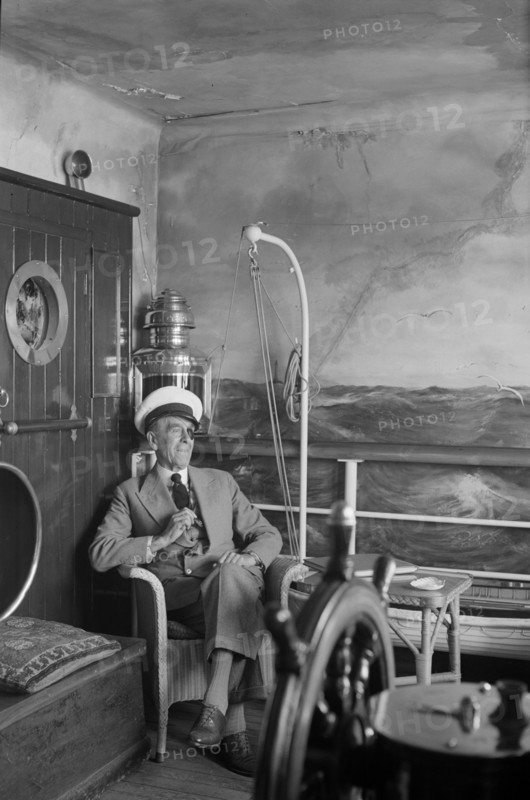 A man in a sailor's cap and eyepatch sits in a reconstructed ship's cabin, c1945-c1965
