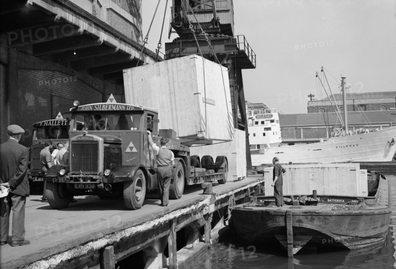 A large crate is hoisted from a lorry onto a barge at the West Quay, Wapping, London, c1945-c1965