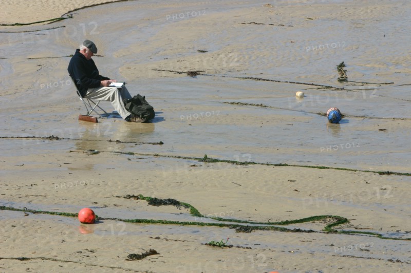 Man sitting on the sand in St Ives harbour at low tide, Cornwall