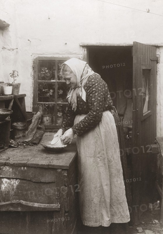 A woman in apron and headscarf washing up a mug outside her home, Landskrona, Sweden, 1910. Artist: Unknown