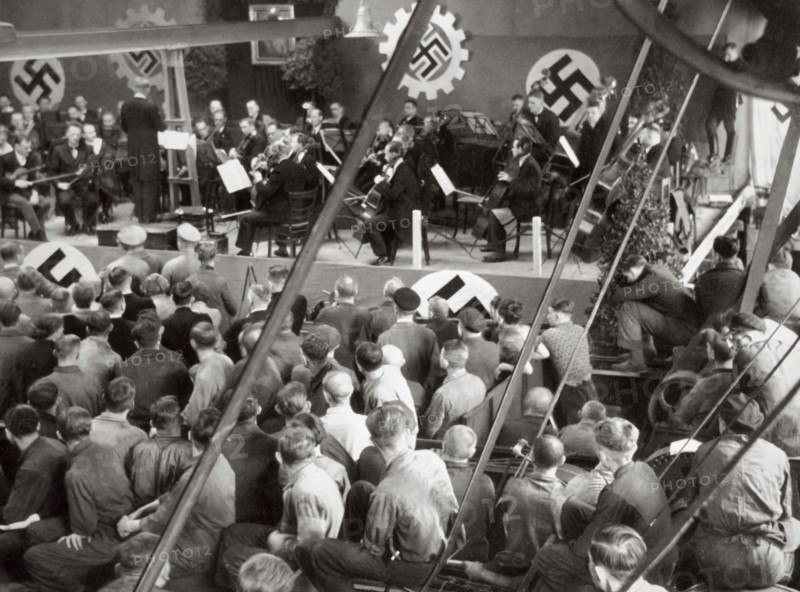 An orchestra plays to some factory workers as they take a break from work, Germany, 1936. Artist: Unknown