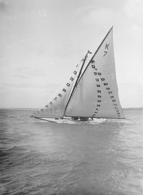 The 7 Metre 'Ginerva' (K7) under sail with prize flags, 1912. Creator: Kirk & Sons of Cowes.