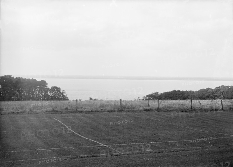 View of a tennis court and the sea, c1935. Creator: Kirk & Sons of Cowes.