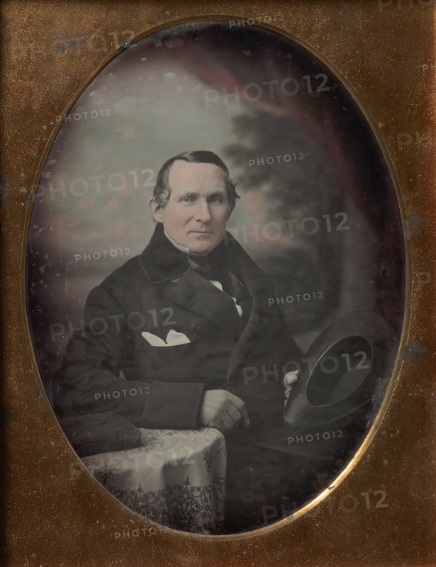 Man Wearing Coat and Gloves, Holding Hat, Seated in Front of Painted Outdoor Backdrop, 1840s.